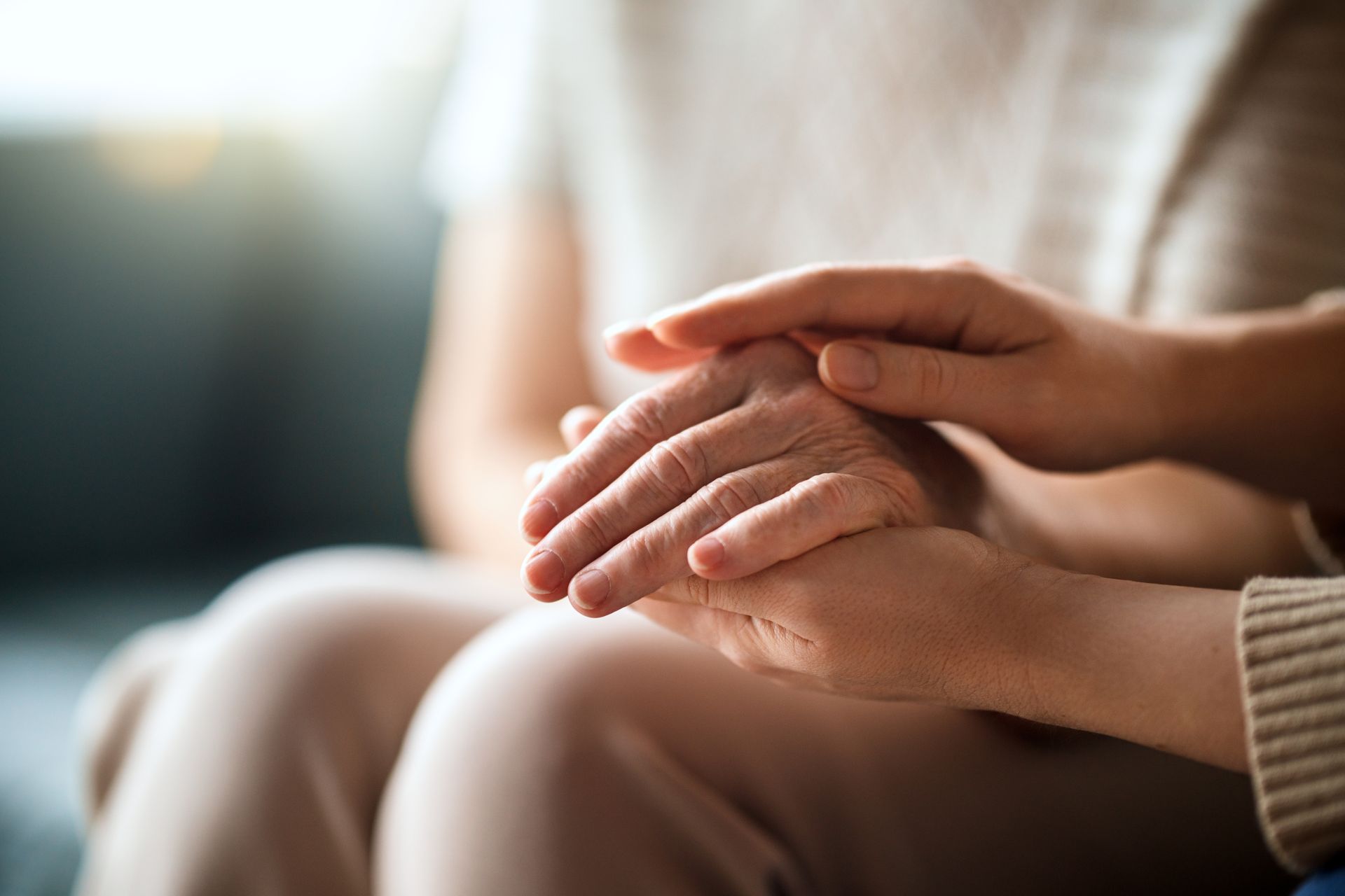 Hands resting gently together in a softly lit, blurred indoor setting