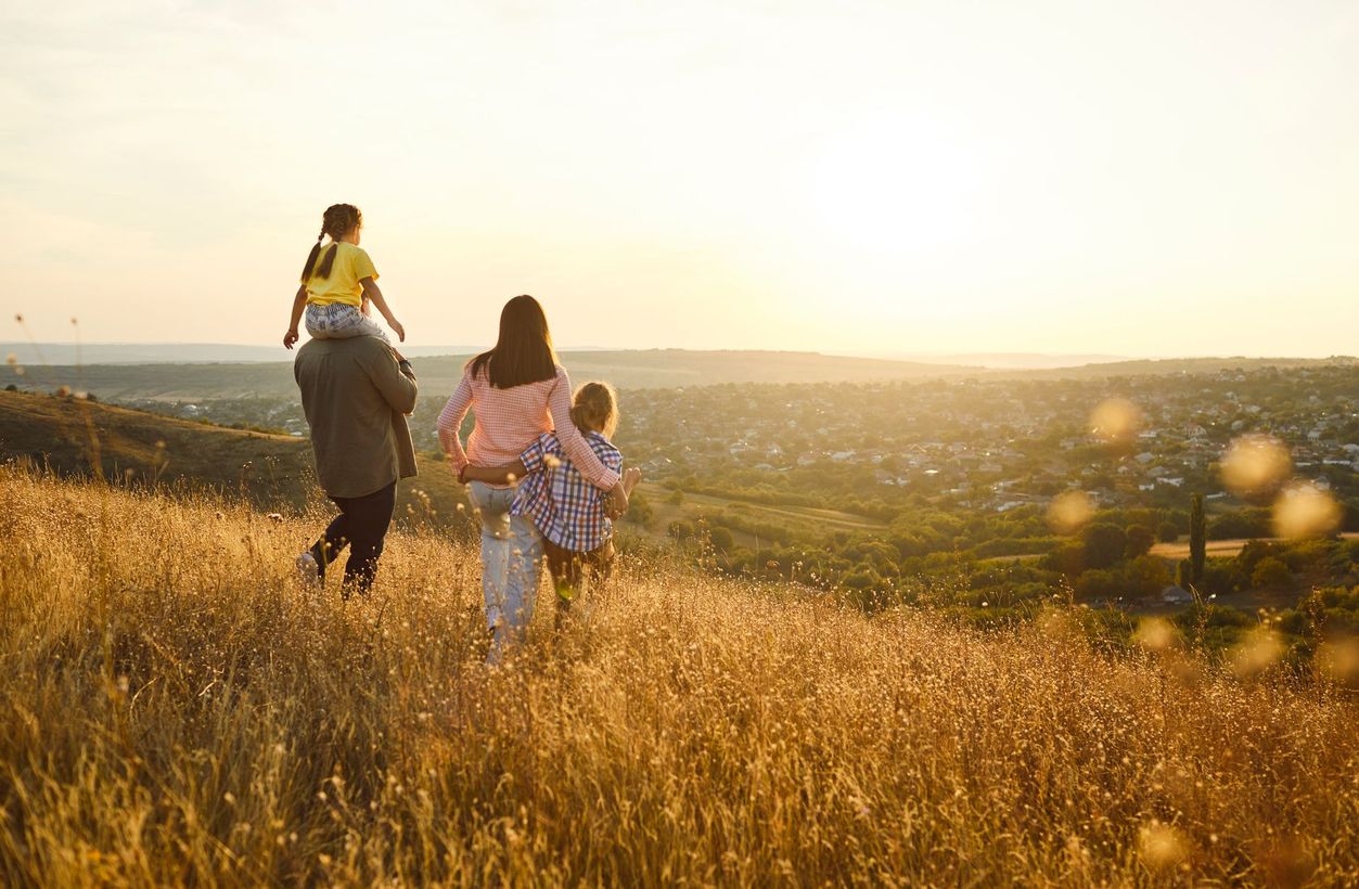 Three people walking through a golden field at sunset, with a wide landscape in the background