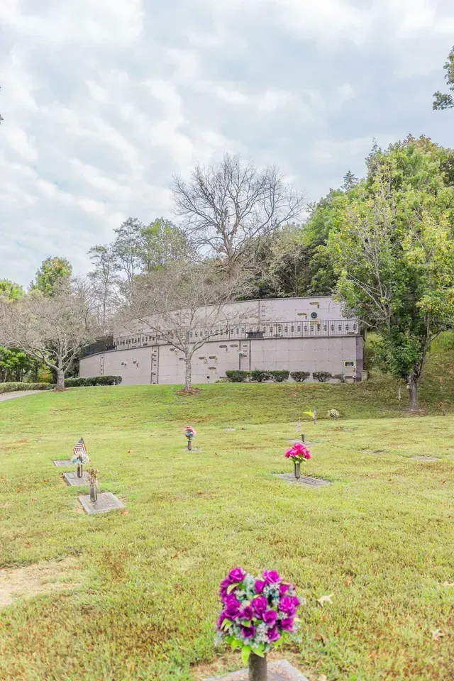 Grassy cemetery with colorful flower arrangements and a mausoleum under cloudy sky
