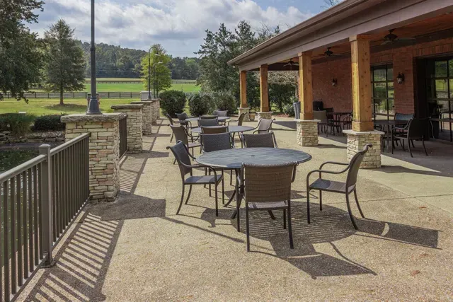 Outdoor patio with tables and chairs beside a stone wall, overlooking a green landscape.