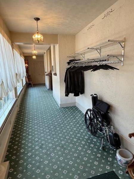 A hallway with green patterned carpet, pendant lights, a wall-mounted coat rack with hangers, and a folded wheelchair.