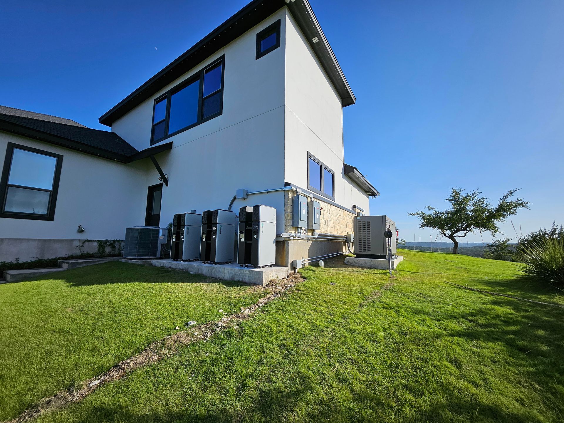 White two-story house with large windows and a green lawn under a clear blue sky.