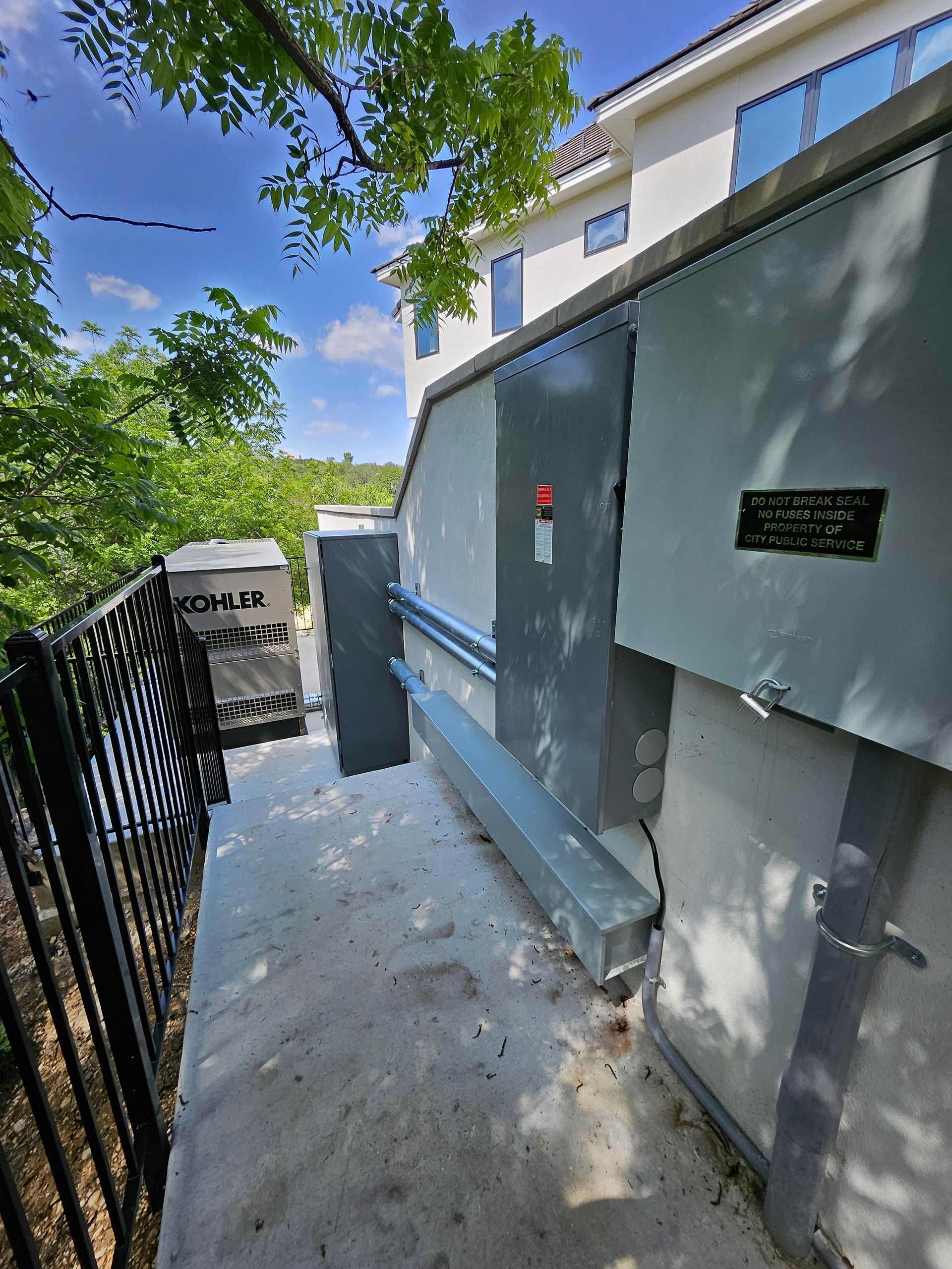Concrete walkway beside gray building and black metal gate under leafy trees