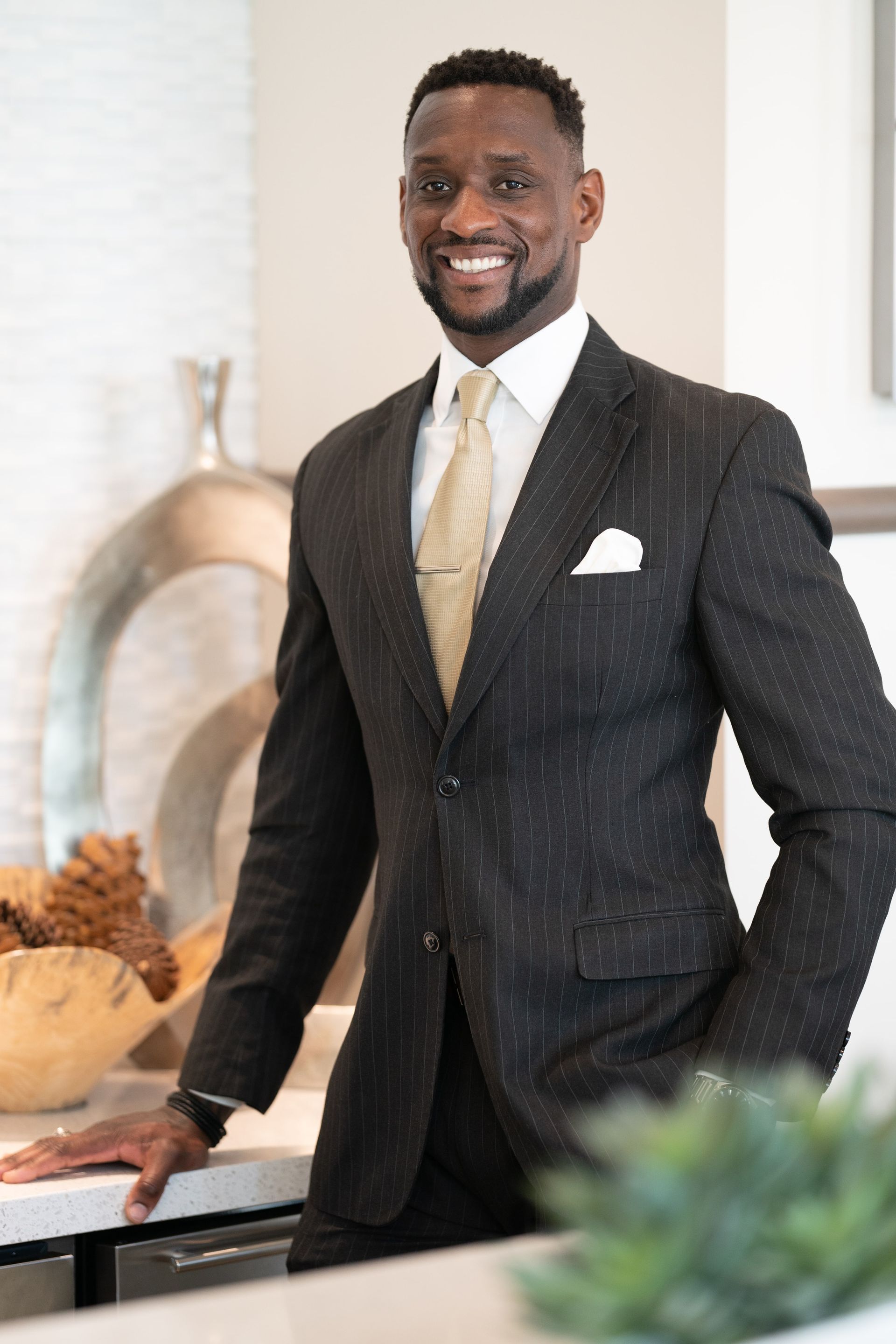 A man in a suit and tie is standing in a kitchen with his hands in his pockets.