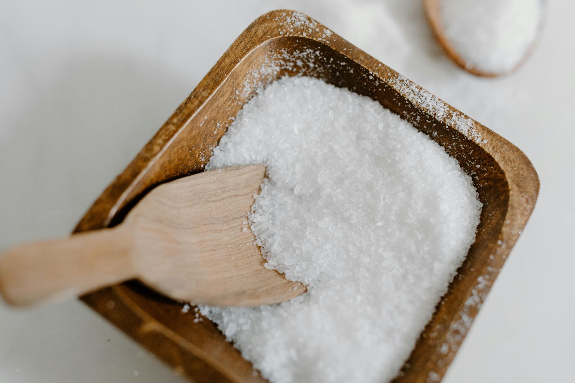 Wooden bowls filled with white sugar and a wooden scoop.