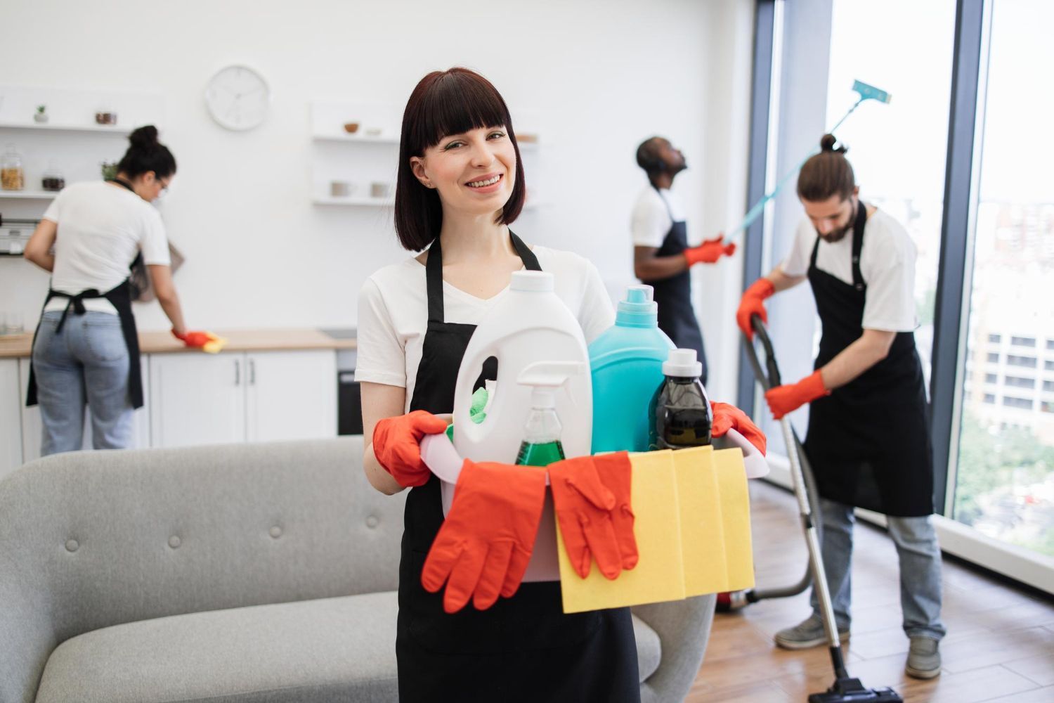 Cleaning crew with supplies in a bright office; one person holds a yellow caddy and smiles.