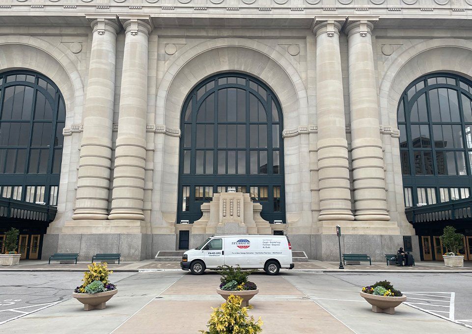 Grand stone building facade with arched windows, a white van, and potted flowers in front