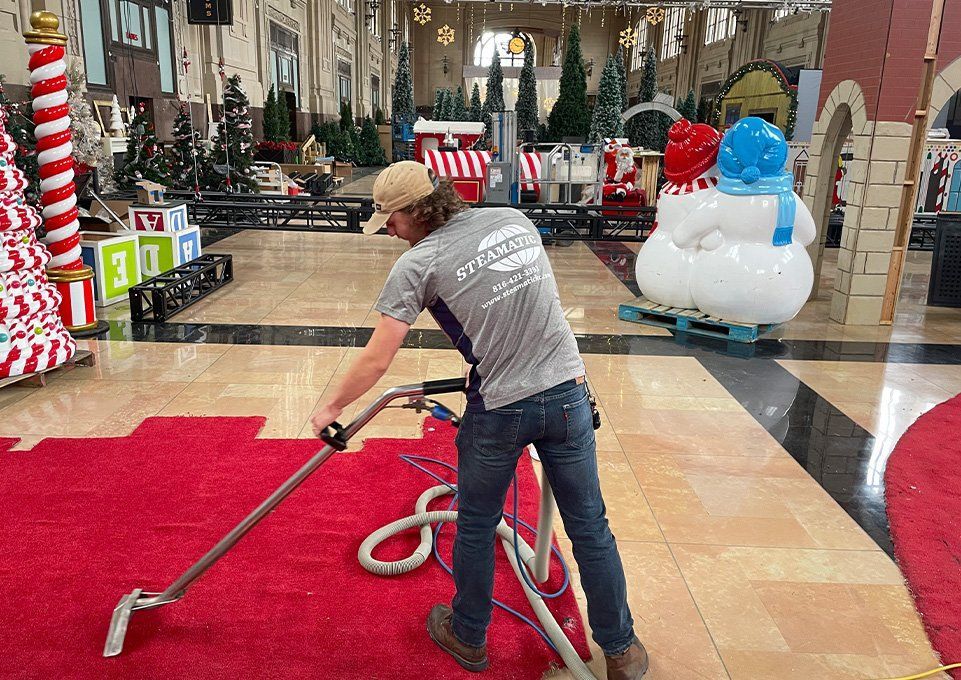 Worker vacuuming a mall’s red carpet near holiday decorations and inflatable snowmen