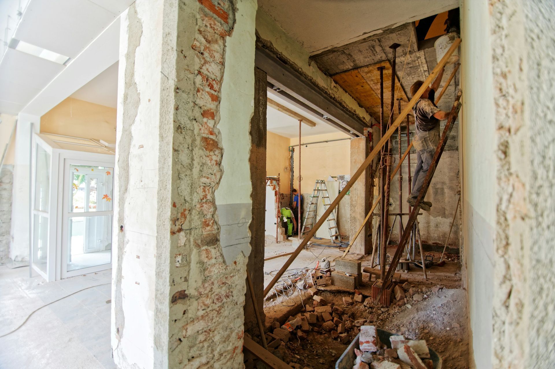Worker in protective suit spraying disinfectant along a wall with a spray wand.
