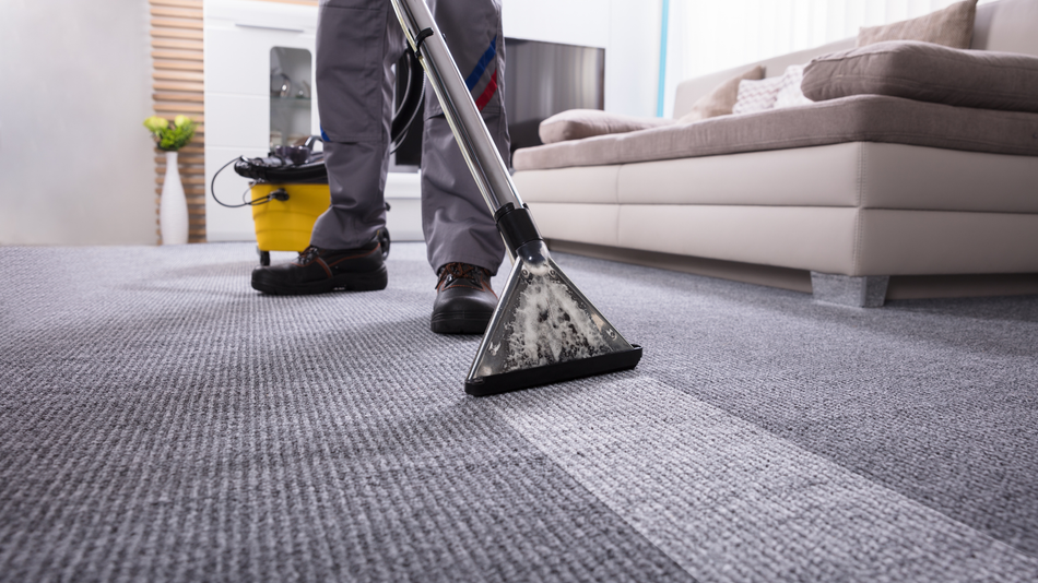 A man is using a vacuum cleaner to clean a carpet in a living room.