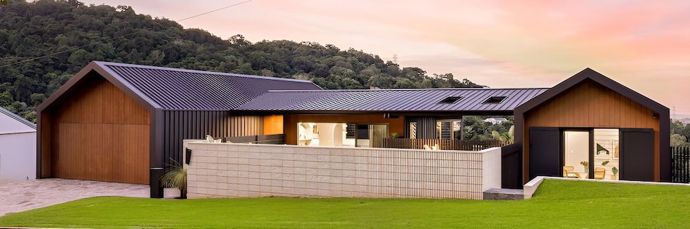 A Large House With a Black Roof is Sitting on Top of a Lush Green Hillside — Andergrove Plumbing & Drainage Pty Ltd In Richmond, QLD