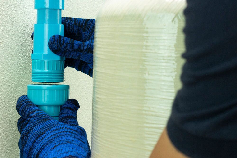 A Person Wearing Blue Gloves is Holding a Blue Pipe — Andergrove Plumbing & Drainage Pty Ltd In Bowen, QLD