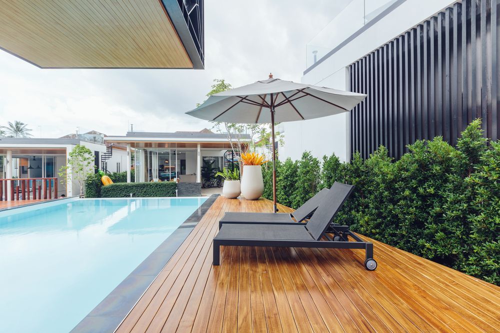 A Swimming Pool With a Wooden Deck and Chairs and an Umbrella — Lismore Poolscene in Clunes, NSW