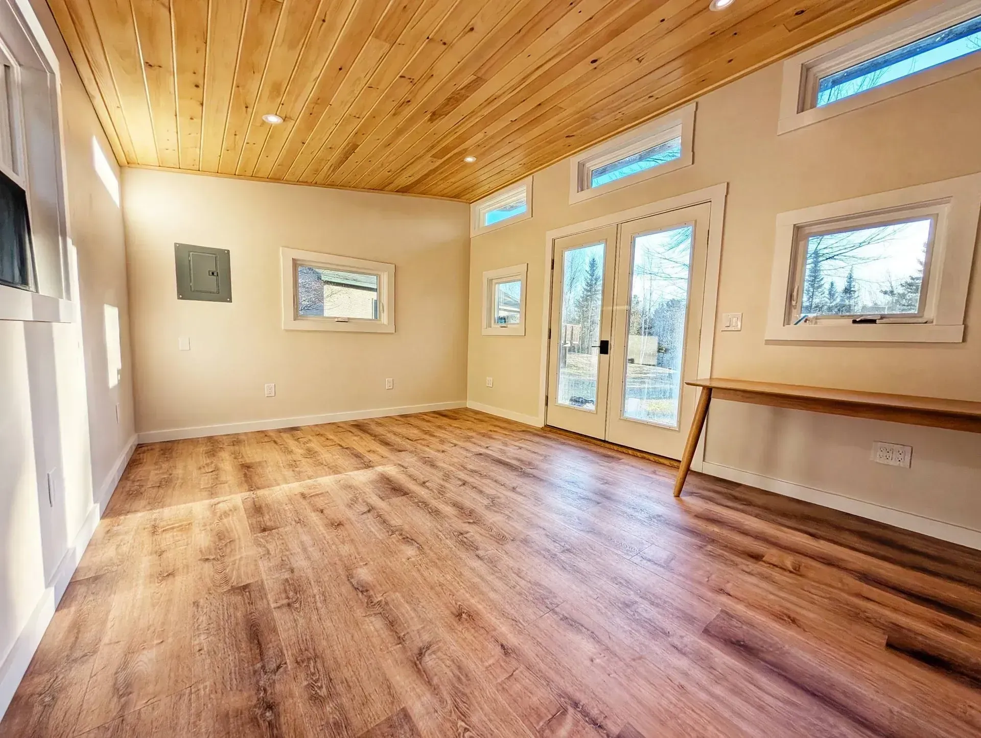 Empty room with wood floor, ceiling, and a desk against the wall; double doors lead outside.