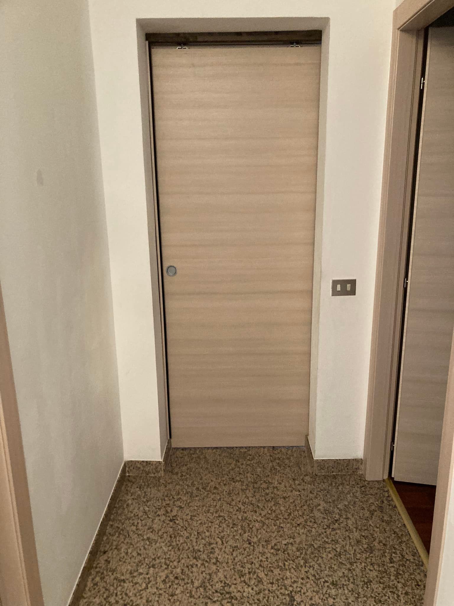 Un corridoio con una porta di legno e un pavimento di marmo.