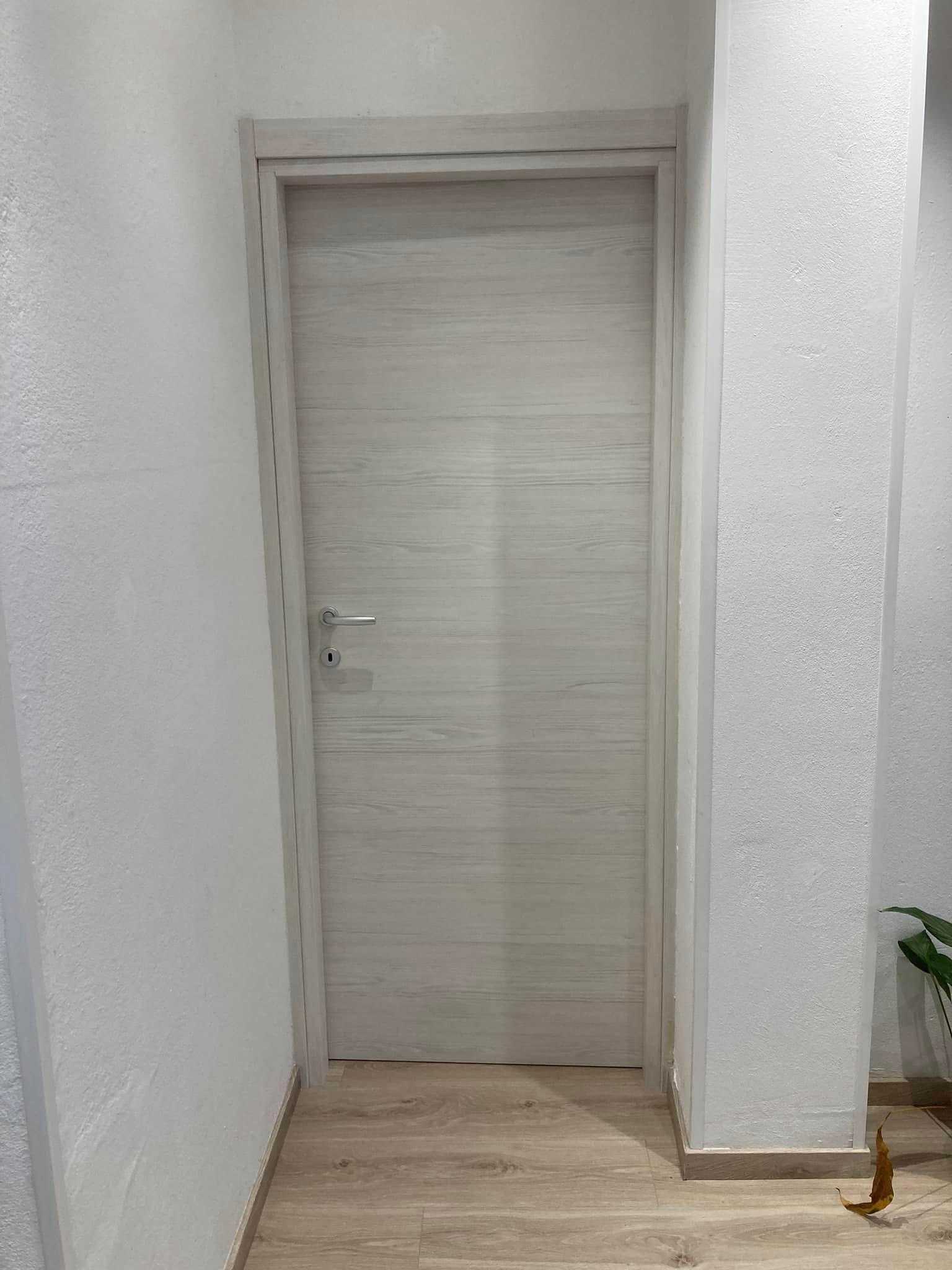 Una porta bianca si trova in un corridoio accanto a un muro bianco.