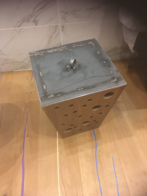 Una scatola di metallo con dei buchi è appoggiata su un pavimento di legno.