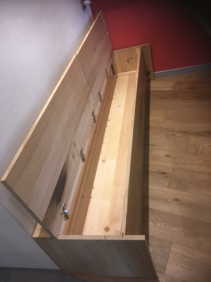 Una panca di legno con il coperchio aperto è appoggiata su un pavimento di legno.