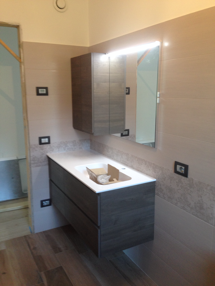 Un bagno con lavandino, specchio e mobiletto.
