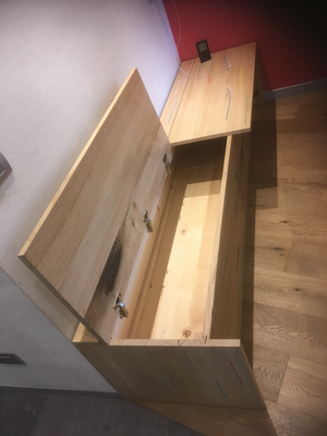 Una panca di legno con il coperchio aperto è appoggiata su un pavimento di legno.