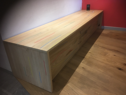 Una panca di legno è appoggiata su un pavimento di legno in una stanza con una parete rossa.