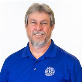 Man wearing a blue polo shirt smiles, looking at the camera. He has grey hair and a beard.