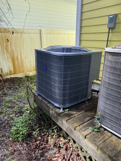 New Carrier air conditioning unit next to an older unit on a wooden platform beside a yellow house.