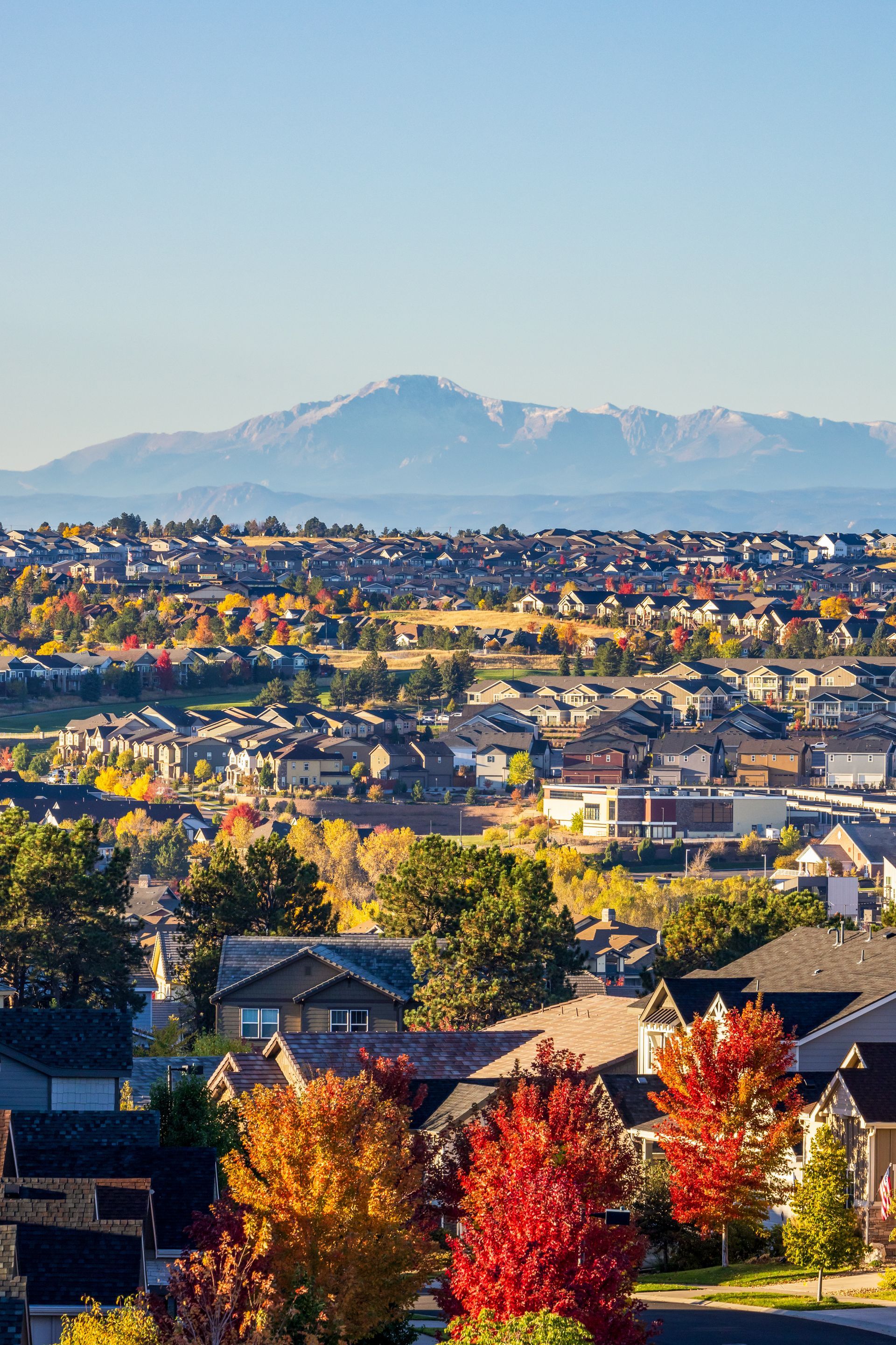 Suburban neighborhood with colorful autumn trees and distant snow-capped mountains under a clear sky