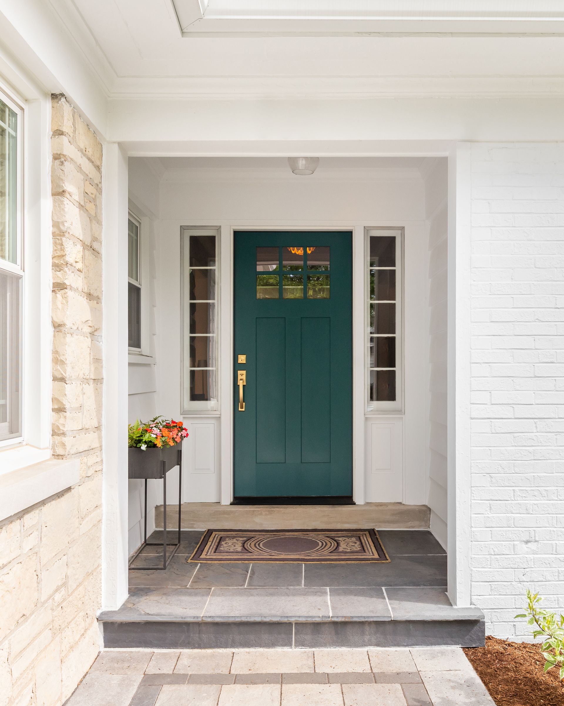 Front porch with teal front door, white walls, steps, and a small flower table.