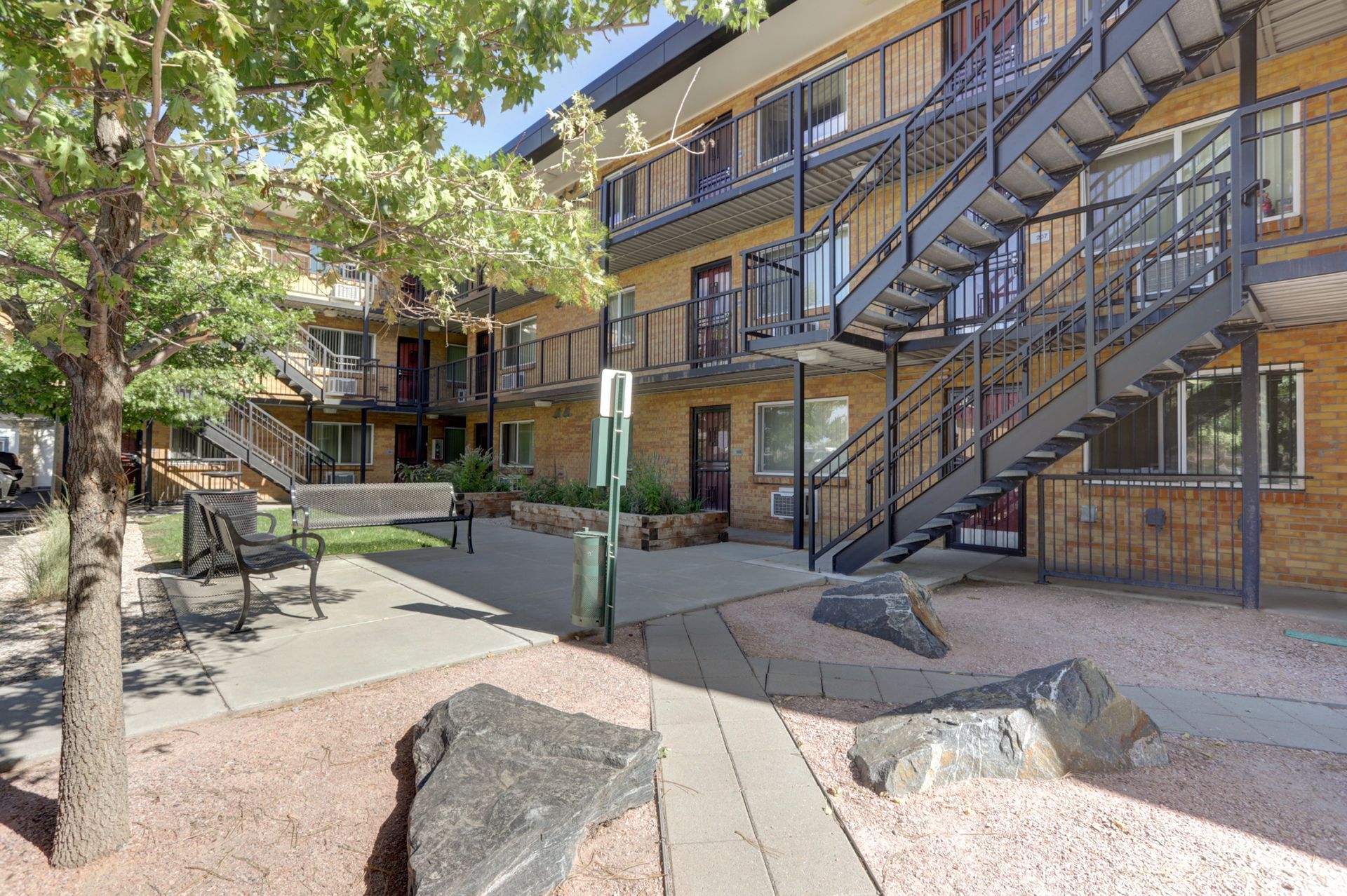 Apartment courtyard with trees, benches, and exterior staircases on a brick building