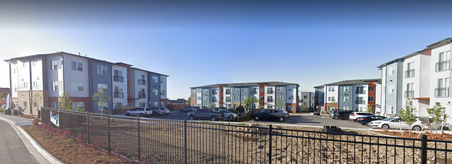 Apartment buildings behind a metal fence under a clear blue sky