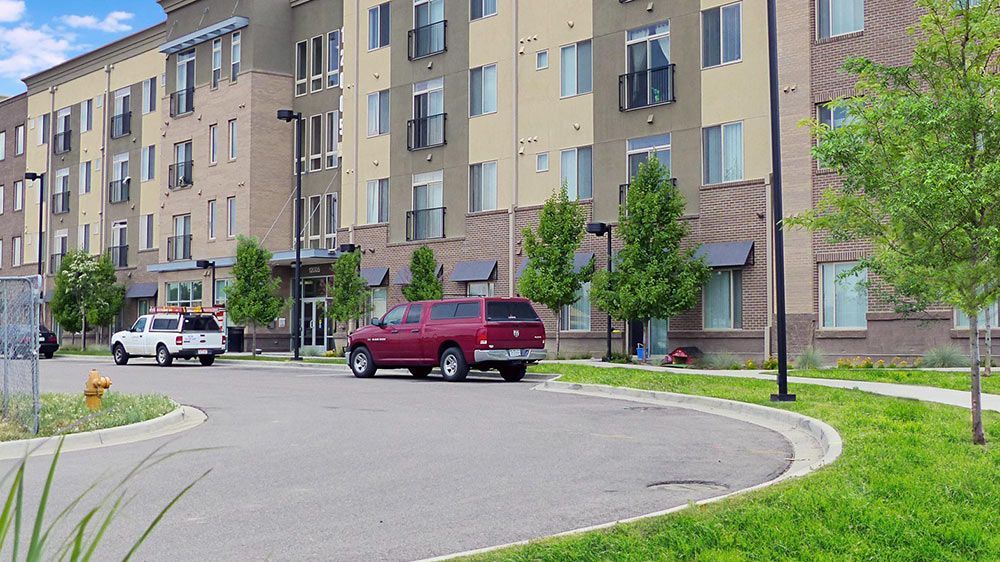 Apartment building courtyard with parked cars and a curved street, viewed from the sidewalk