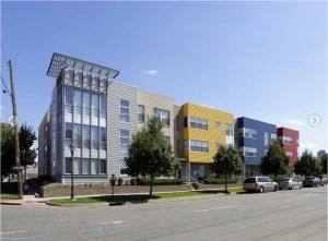 Modern office building with glass tower, colorful facade panels, and a parked car along the street