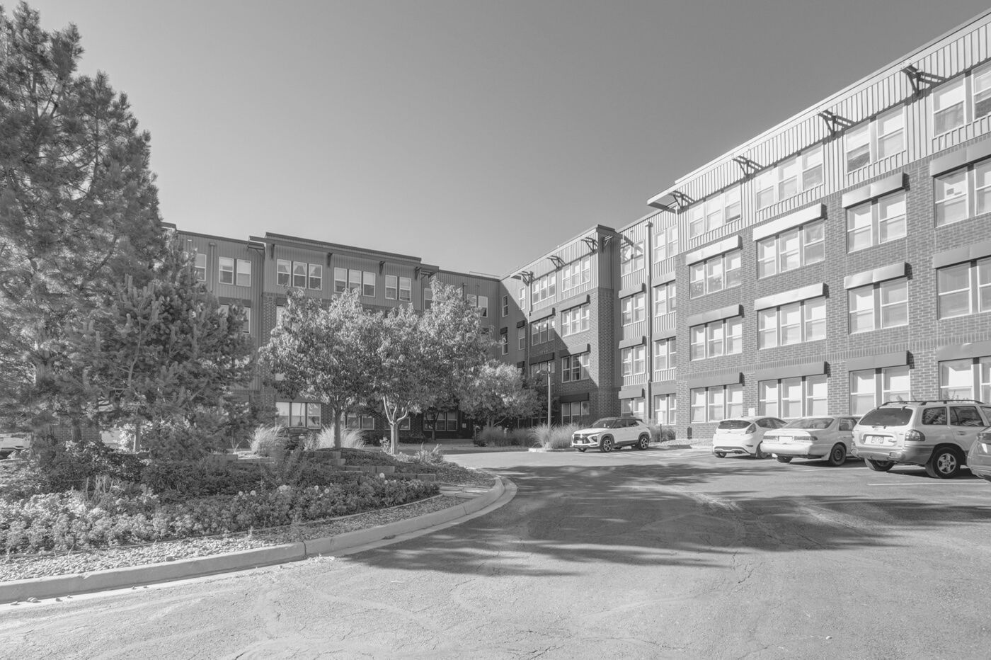 Courtyard of a brick apartment building with parked cars and trees on a sunny day