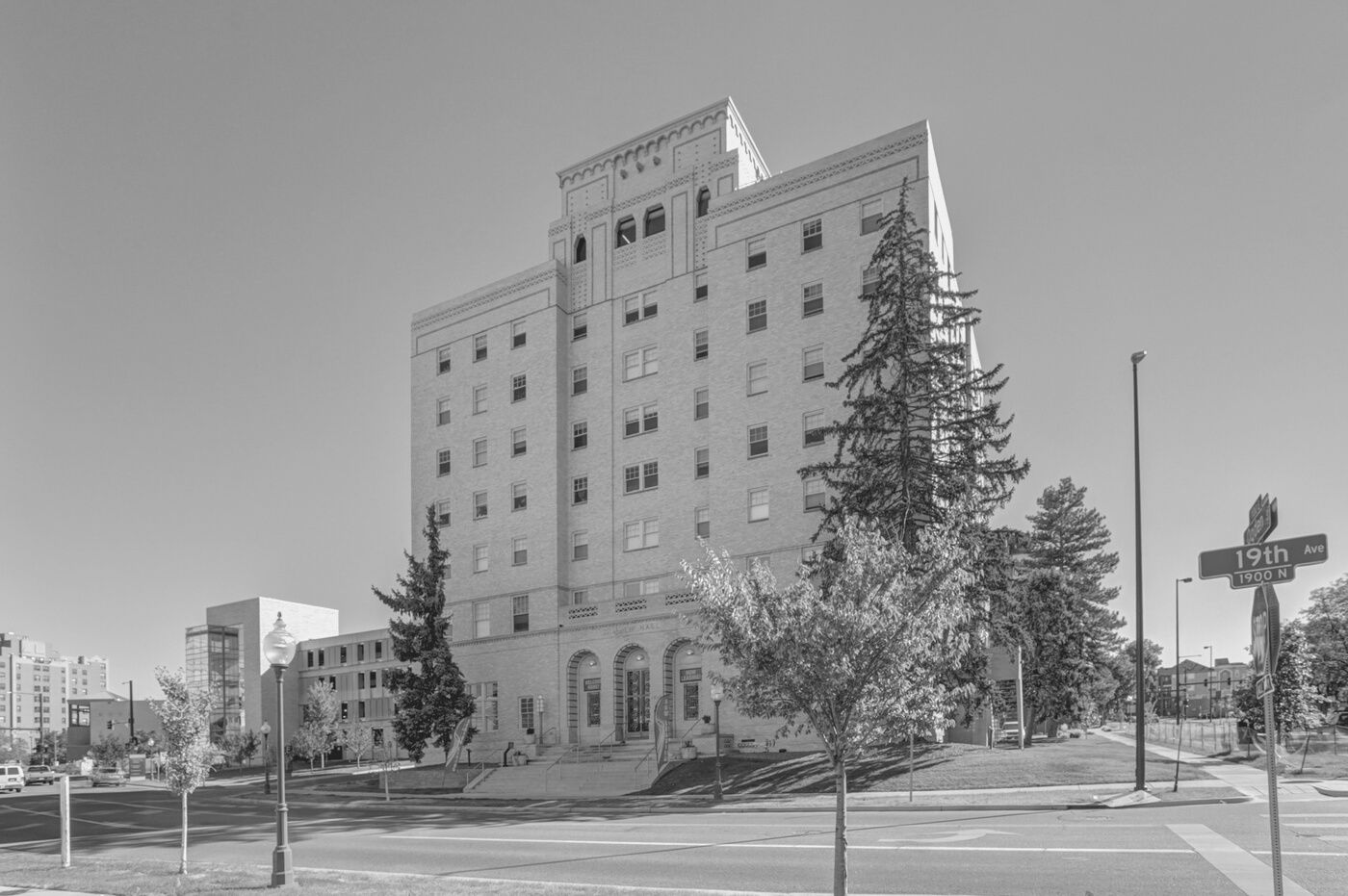 Historic multistory building with trees and a roadside cross under a clear sky