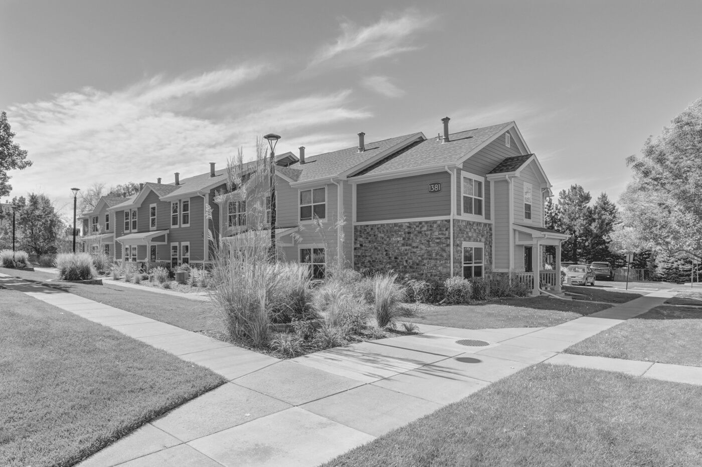 Apartment building with brick and siding exterior, sidewalk, grass, and shrubs under a bright sky