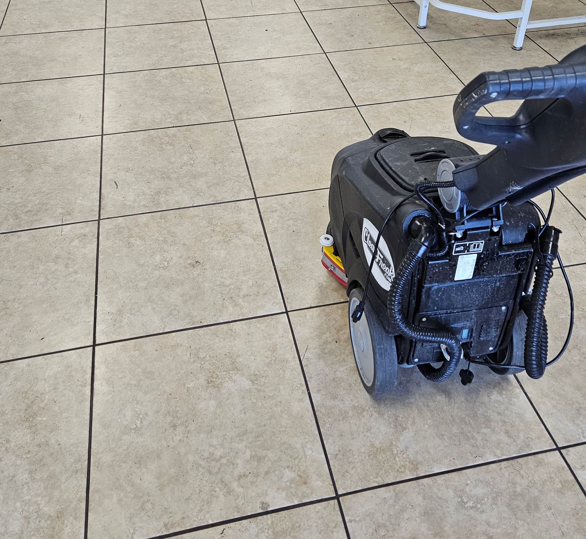 Black wheelchair on a tan tiled floor near a table and chair.