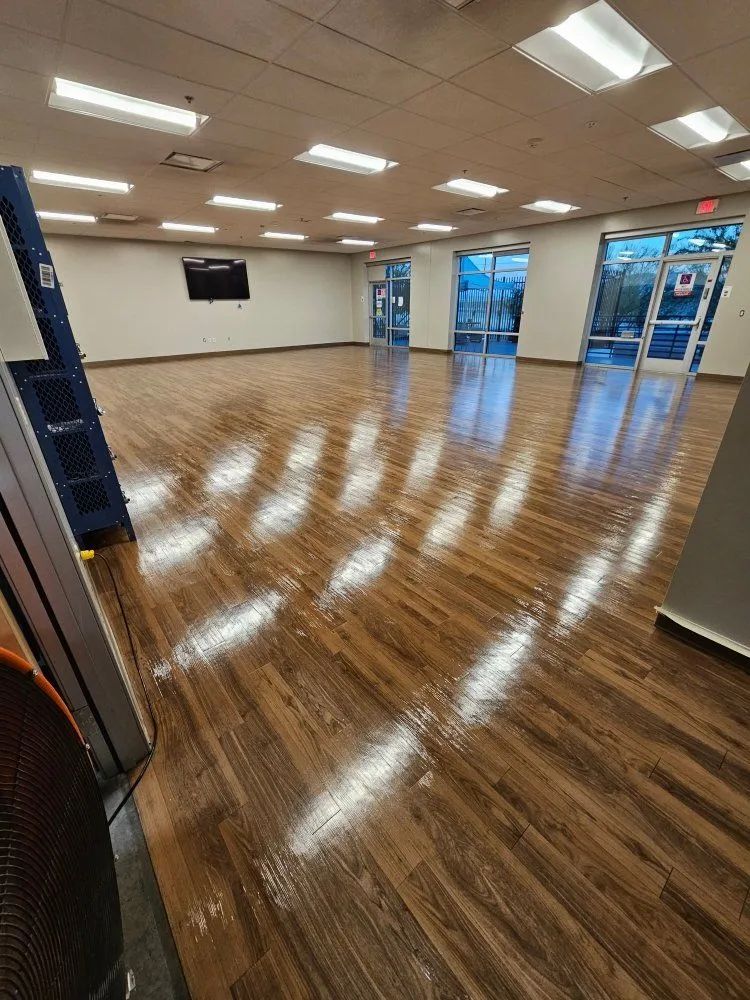 Empty bright room with polished wood floor, white walls, ceiling lights, and glass entry doors