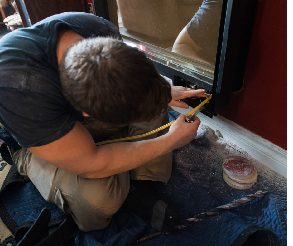 A person kneels, measuring a dark window frame with a yellow tape measure. They are working near the floor against a red wall.