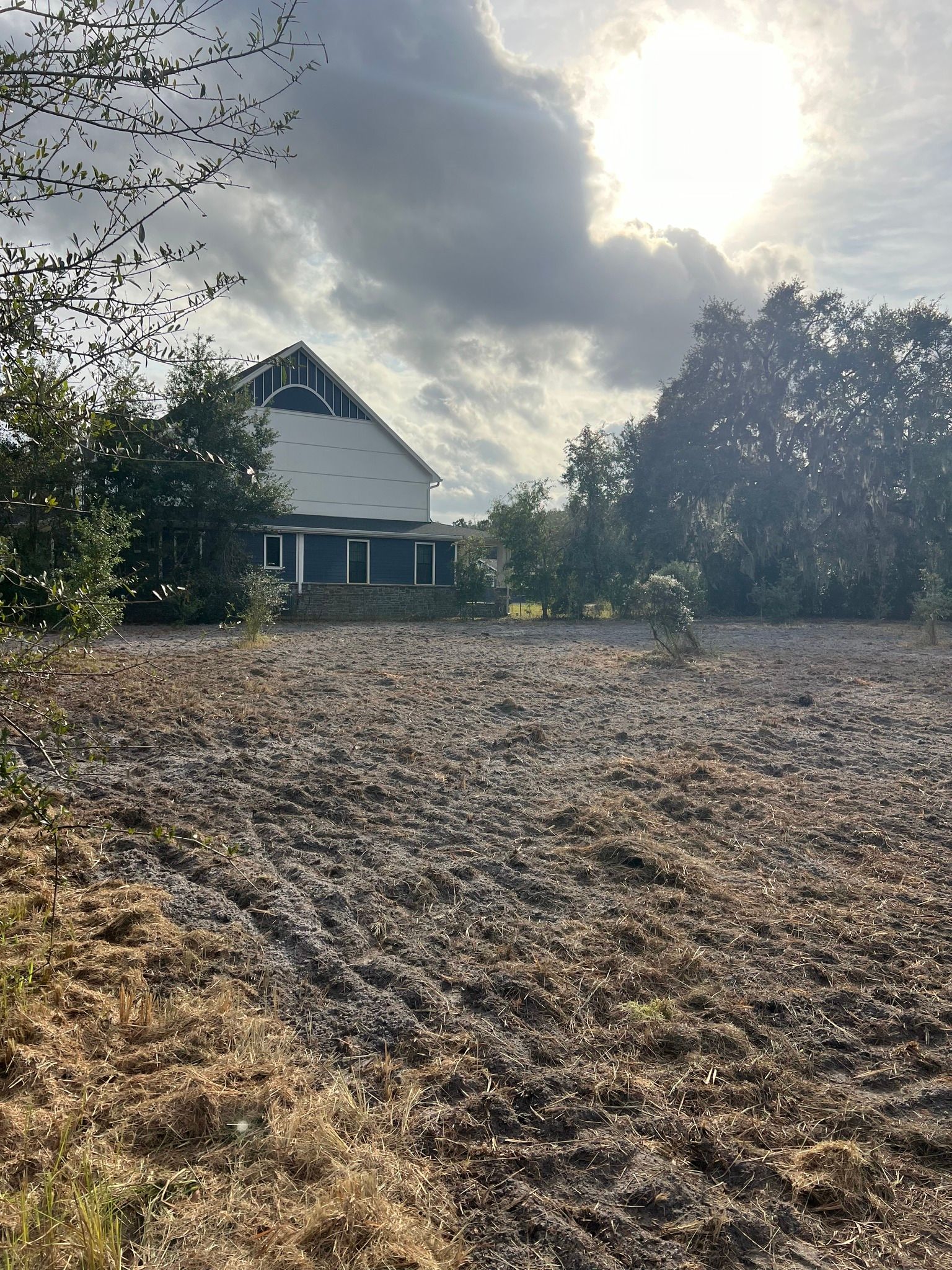 House behind a field of dry grass, with trees and a cloudy sky.