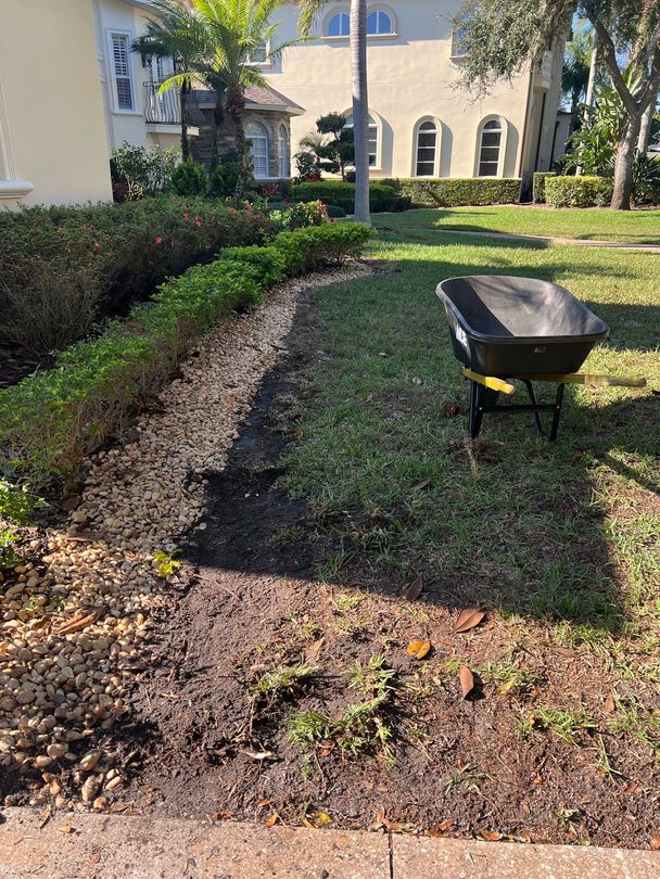 A black wheelbarrow on grass near a landscaped garden bed filled with dark soil.