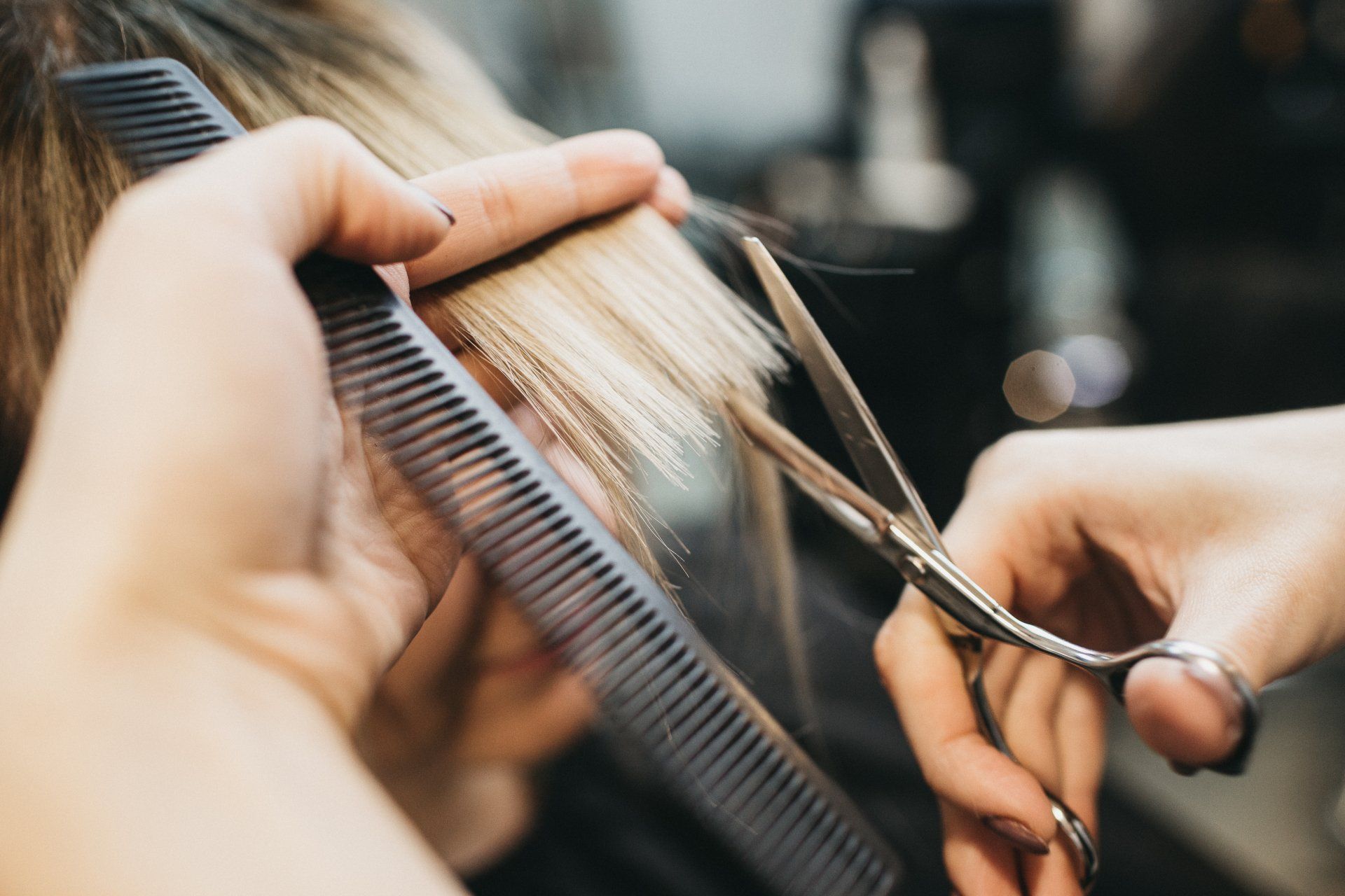 Hairdresser cutting blonde hair with scissors and comb.
