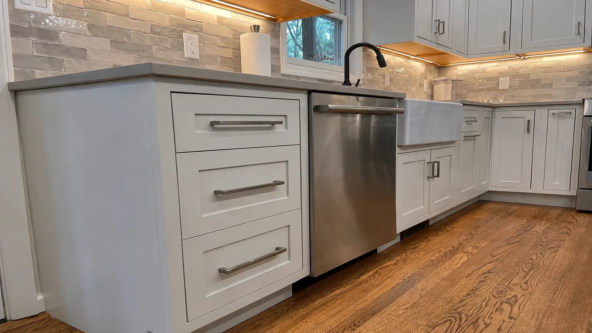 Modern white kitchen with stainless steel dishwasher and wood flooring