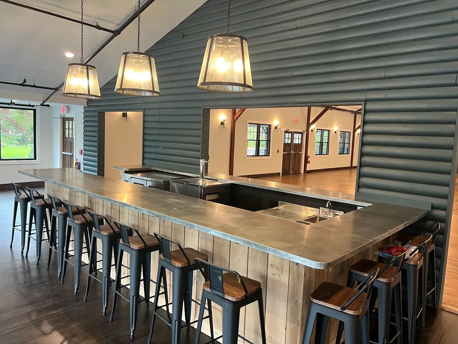 Long wooden bar table with stools under hanging lights in a modern rustic dining space