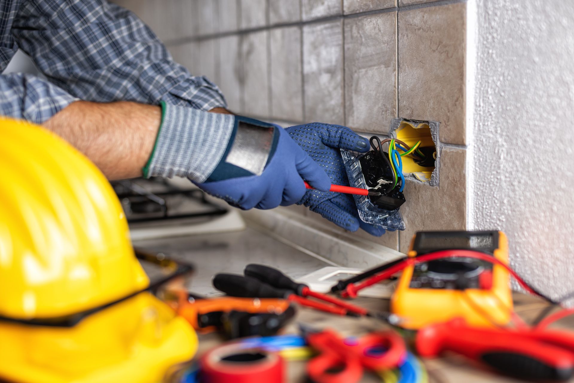 Electrician using screwdriver to wire wall outlet with tools on counter. Electrician using screwdriver to wire wall outlet with tools on counter.