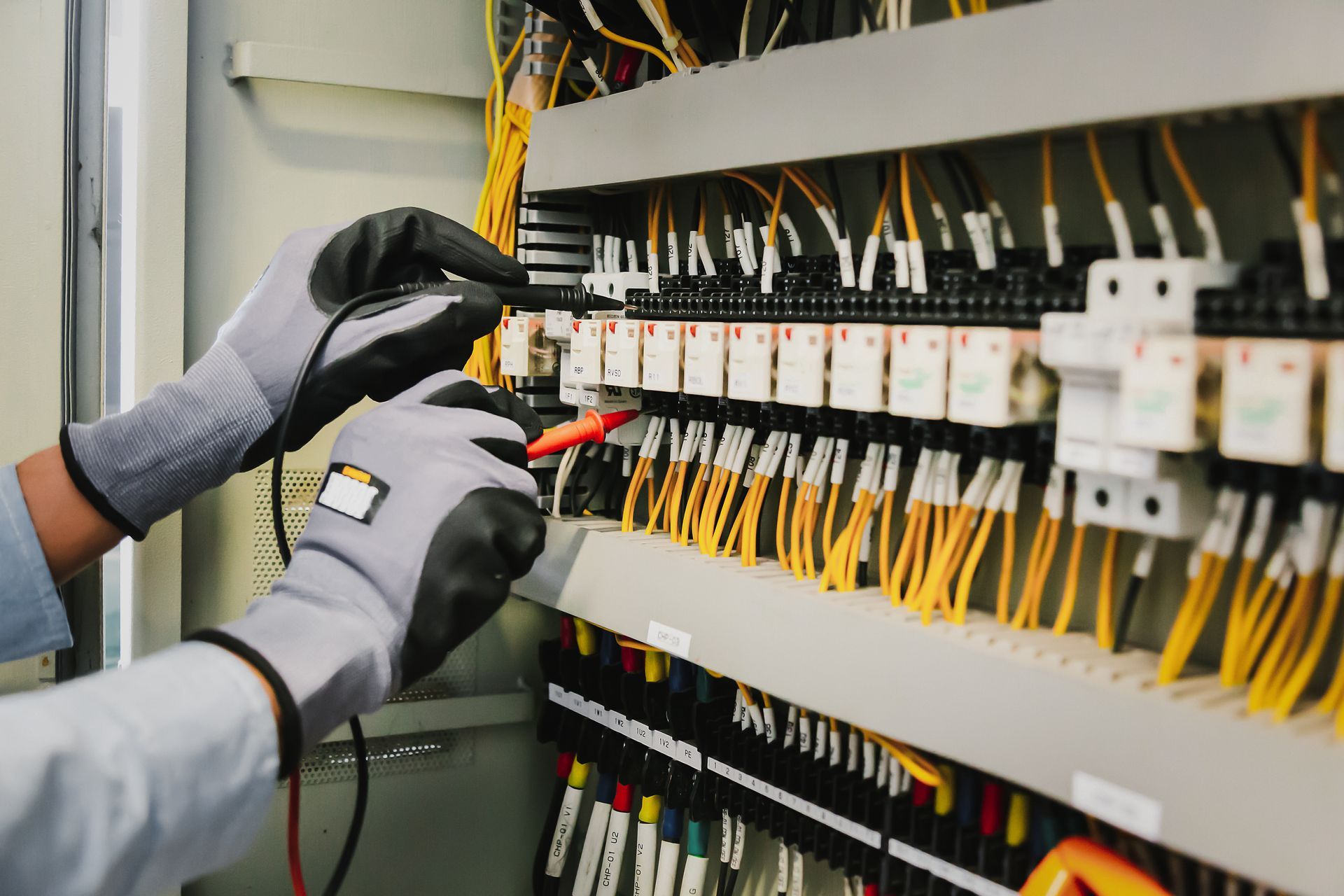 Hands wearing gloves testing electrical wiring in a panel.
