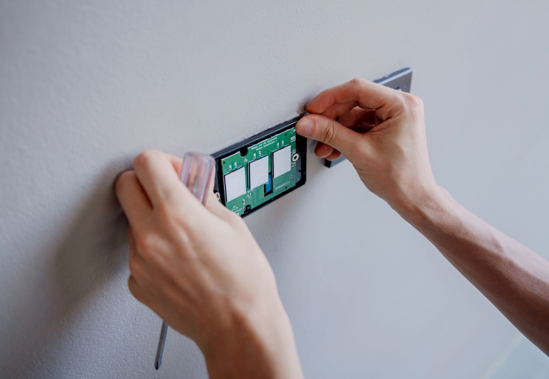 Hands installing a circuit board onto a wall.