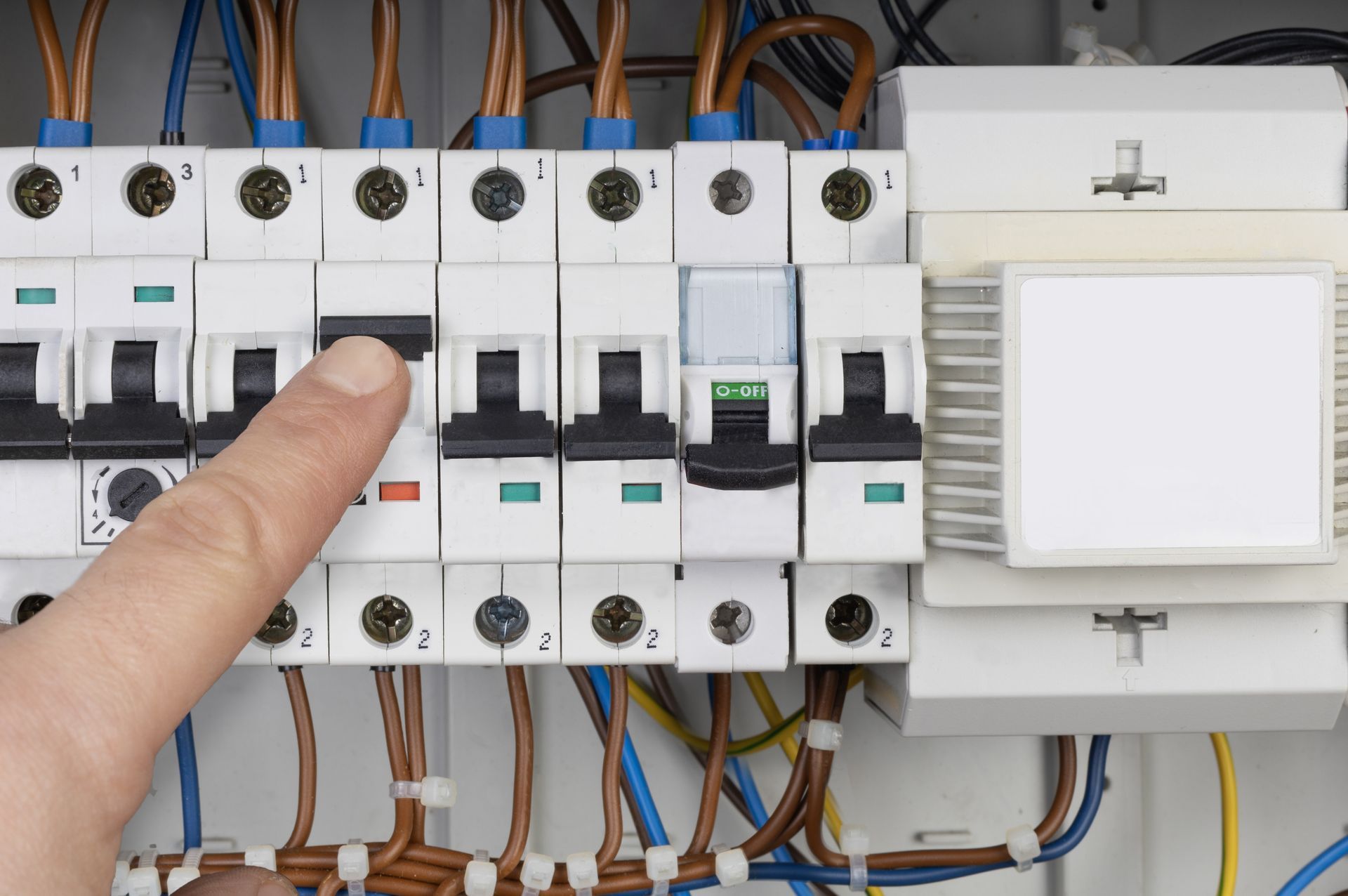 Hand pressing a circuit breaker in an electrical panel, wires visible.