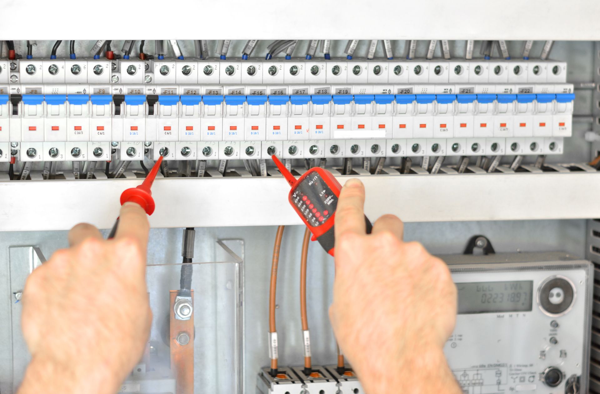 Electrician testing circuit breakers in panel with voltage tester for maintenance work.
