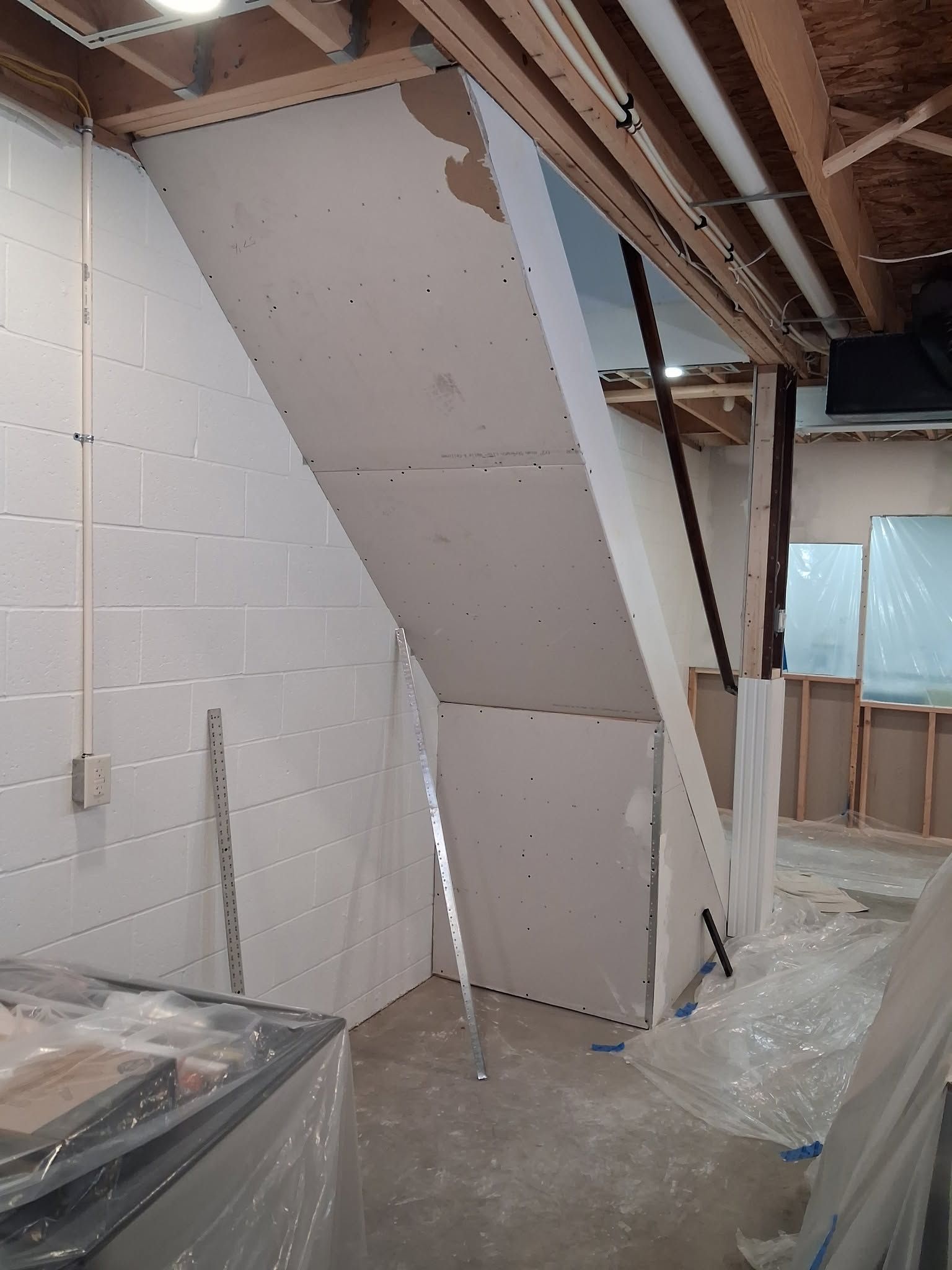 Partially built drywall stair enclosure in an unfinished basement with exposed framing and insulation